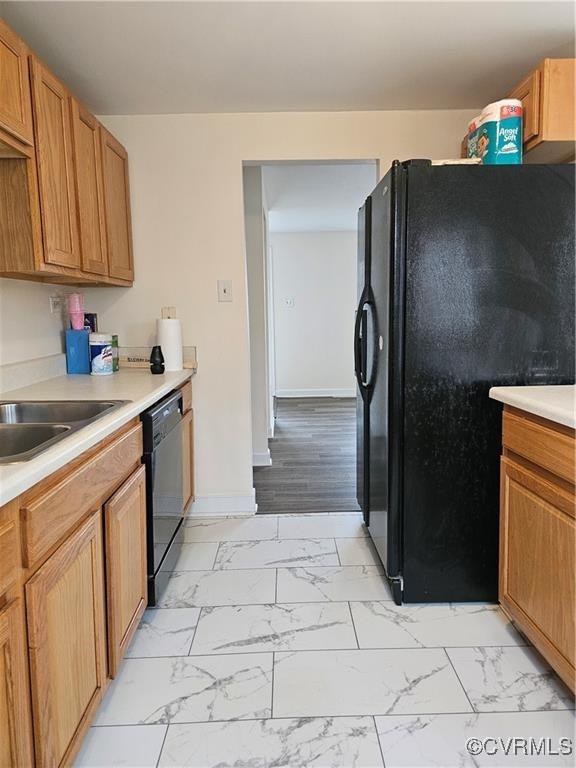 kitchen with baseboards, light countertops, marble finish floor, black appliances, and a sink