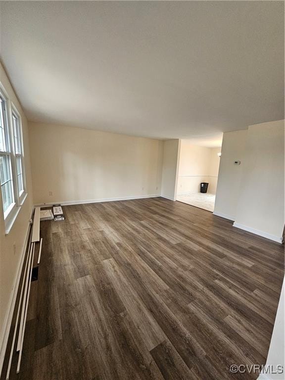 unfurnished living room featuring a baseboard heating unit, baseboards, and dark wood-style flooring