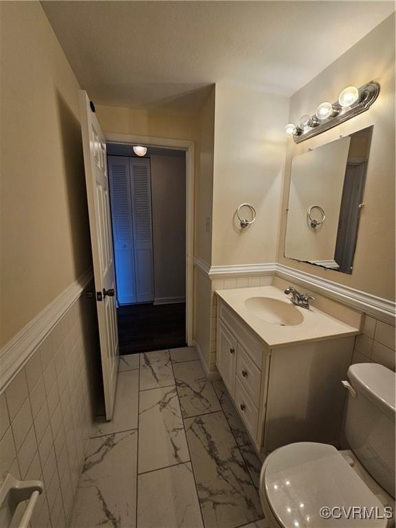 bathroom featuring tile walls, toilet, wainscoting, marble finish floor, and vanity