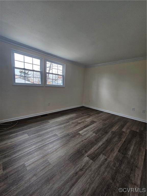 spare room with baseboards, dark wood finished floors, and crown molding