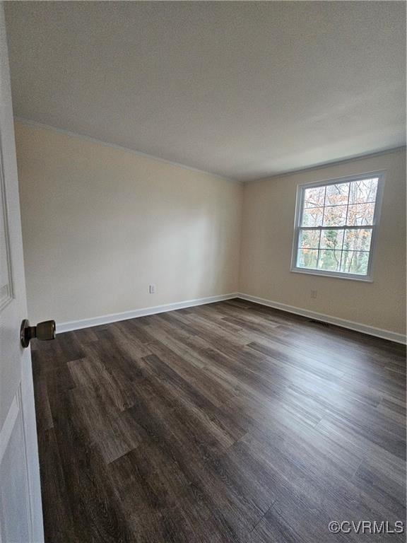 spare room with baseboards and dark wood finished floors