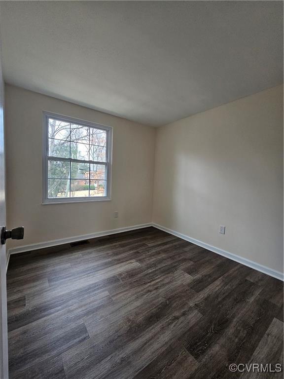 spare room featuring dark wood finished floors, visible vents, and baseboards