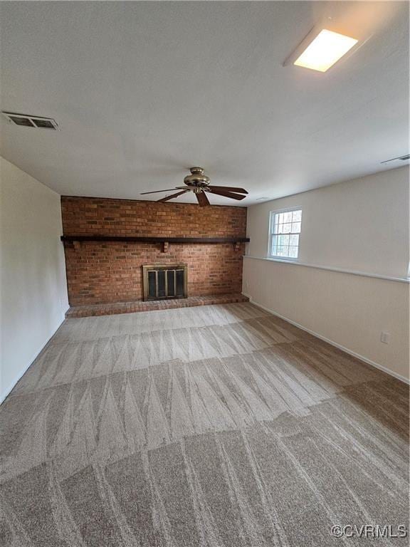 unfurnished living room with visible vents, carpet, brick wall, a brick fireplace, and ceiling fan