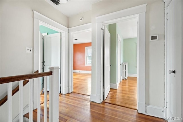 hall with an upstairs landing, wood finished floors, and baseboards