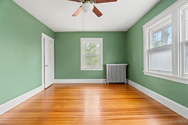 spare room with radiator heating unit, baseboards, light wood finished floors, and ceiling fan