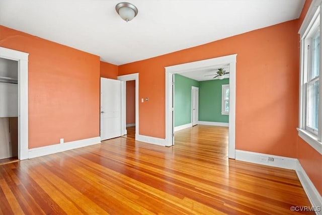 unfurnished room with a wealth of natural light, light wood-type flooring, baseboards, and a ceiling fan