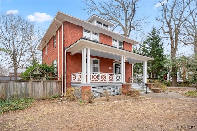 american foursquare style home featuring brick siding, covered porch, and fence