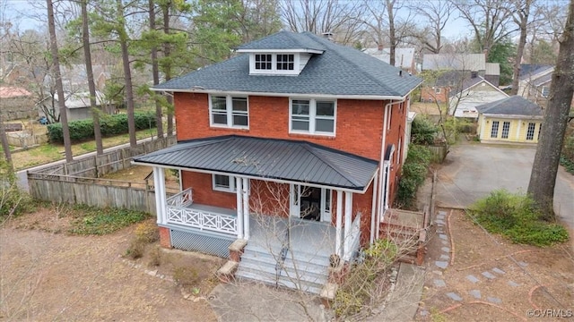 american foursquare style home with brick siding, covered porch, roof with shingles, and fence