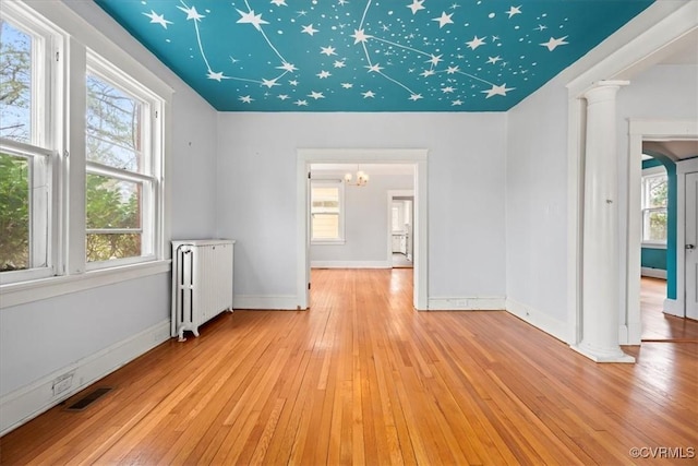 unfurnished room featuring a wealth of natural light, radiator heating unit, light wood-style floors, and decorative columns