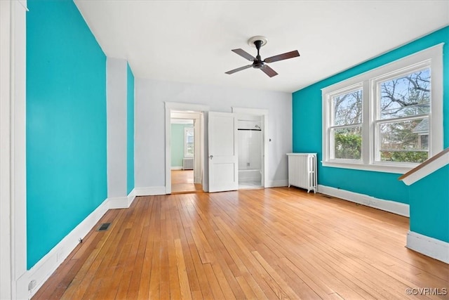 unfurnished bedroom featuring baseboards, wood-type flooring, radiator, and visible vents