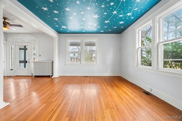 spare room featuring baseboards, visible vents, radiator heating unit, decorative columns, and hardwood / wood-style flooring