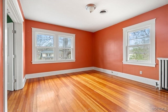 empty room featuring visible vents, baseboards, radiator, and light wood finished floors