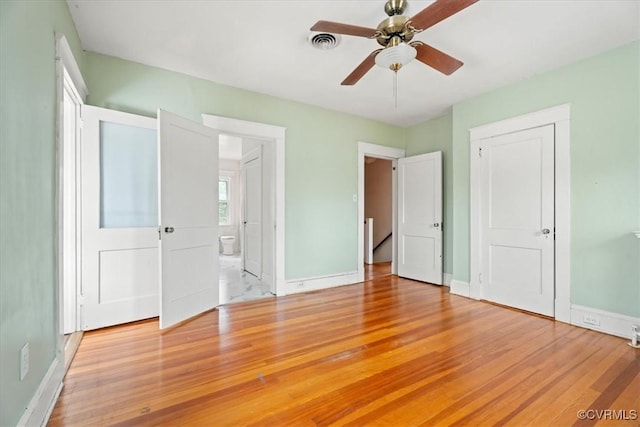 unfurnished bedroom featuring ensuite bath, light wood-style flooring, baseboards, and visible vents