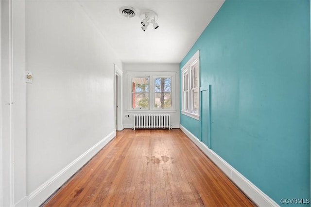 unfurnished room with hardwood / wood-style flooring, radiator, baseboards, and visible vents