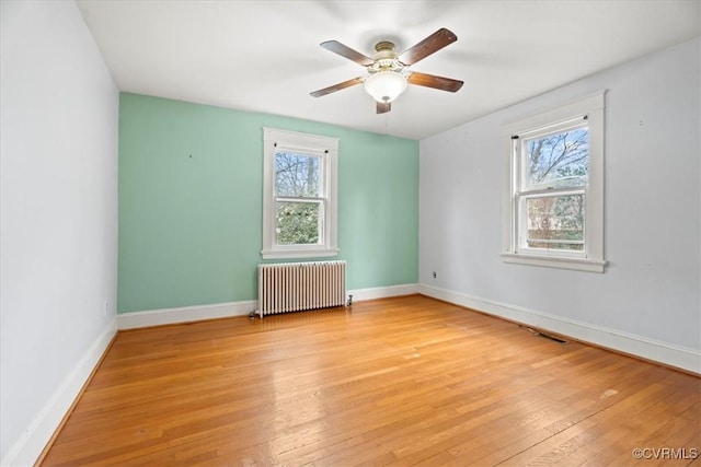 empty room with a wealth of natural light, baseboards, radiator, and light wood-style flooring