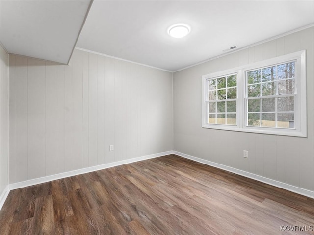 empty room featuring visible vents, crown molding, baseboards, and wood finished floors