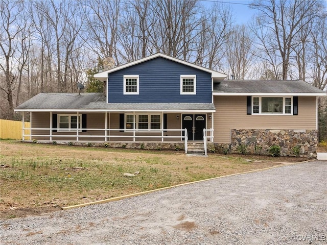 split level home featuring stone siding, a porch, a shingled roof, and a front lawn