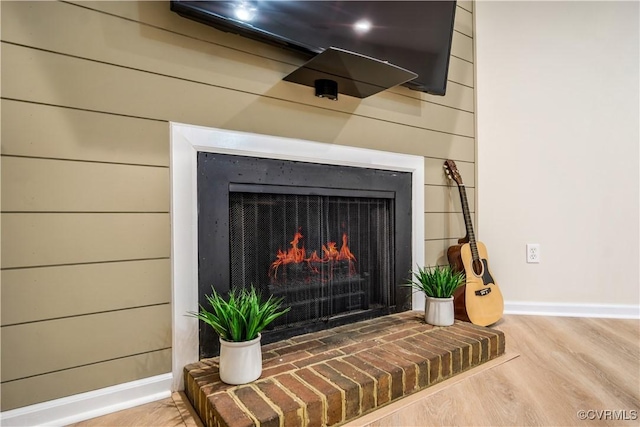 details with baseboards, wooden walls, a warm lit fireplace, and wood finished floors