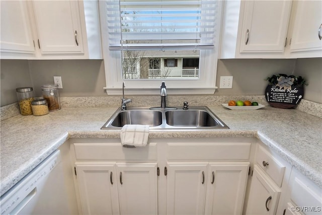 kitchen with white cabinets, light countertops, white dishwasher, and a sink