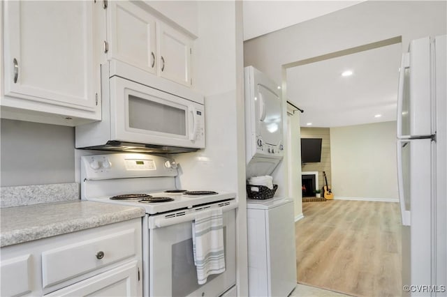 kitchen with white appliances, light countertops, white cabinets, light wood-type flooring, and a large fireplace