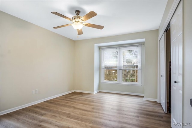 unfurnished bedroom featuring wood finished floors, baseboards, a closet, and ceiling fan