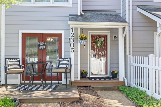 view of exterior entry with a porch, fence, and roof with shingles