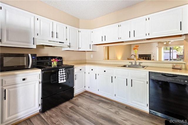 kitchen featuring white cabinets, under cabinet range hood, a sink, and black appliances