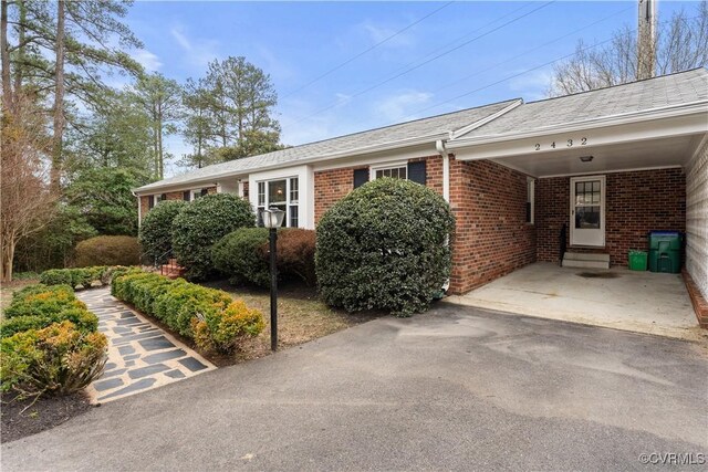 ranch-style house with driveway, a carport, brick siding, and entry steps