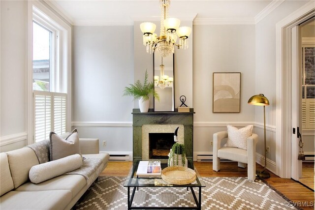 living room with wood finished floors, a fireplace, crown molding, baseboard heating, and a chandelier