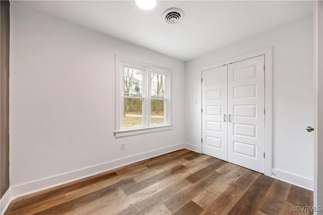 unfurnished bedroom featuring dark wood-style floors, visible vents, a closet, and baseboards