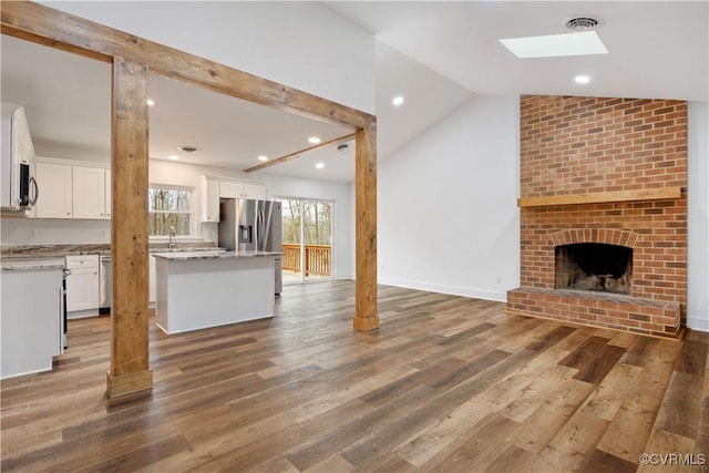 kitchen with visible vents, lofted ceiling with skylight, wood finished floors, open floor plan, and white cabinets