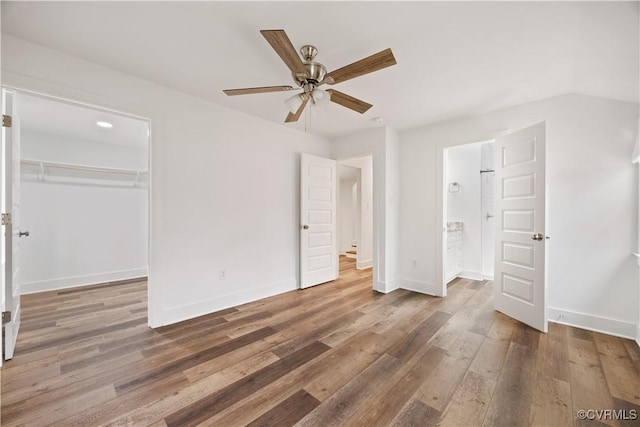 unfurnished bedroom with wood finished floors, baseboards, a closet, a walk in closet, and connected bathroom