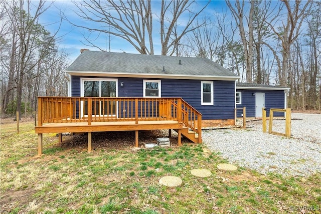 back of house featuring gravel driveway, roof with shingles, and a wooden deck