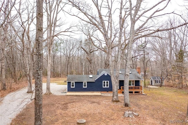 view of front of home featuring aphalt driveway, roof with shingles, a front yard, a chimney, and a deck