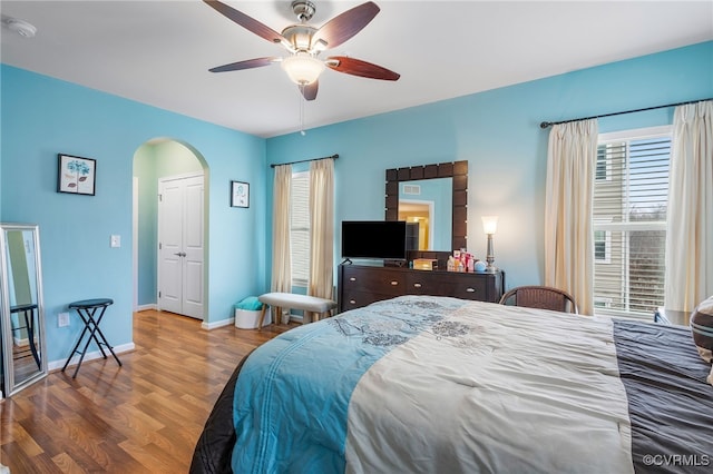 bedroom with ceiling fan, wood finished floors, arched walkways, and baseboards