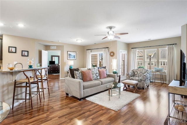 living room with ceiling fan, visible vents, baseboards, and wood finished floors