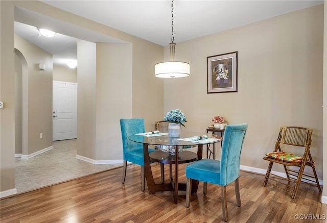 dining area featuring arched walkways, baseboards, and wood finished floors