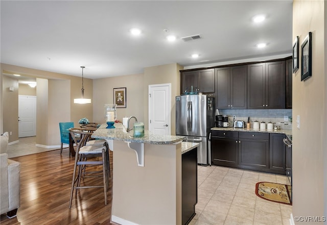 kitchen featuring visible vents, backsplash, light stone countertops, a breakfast bar, and freestanding refrigerator