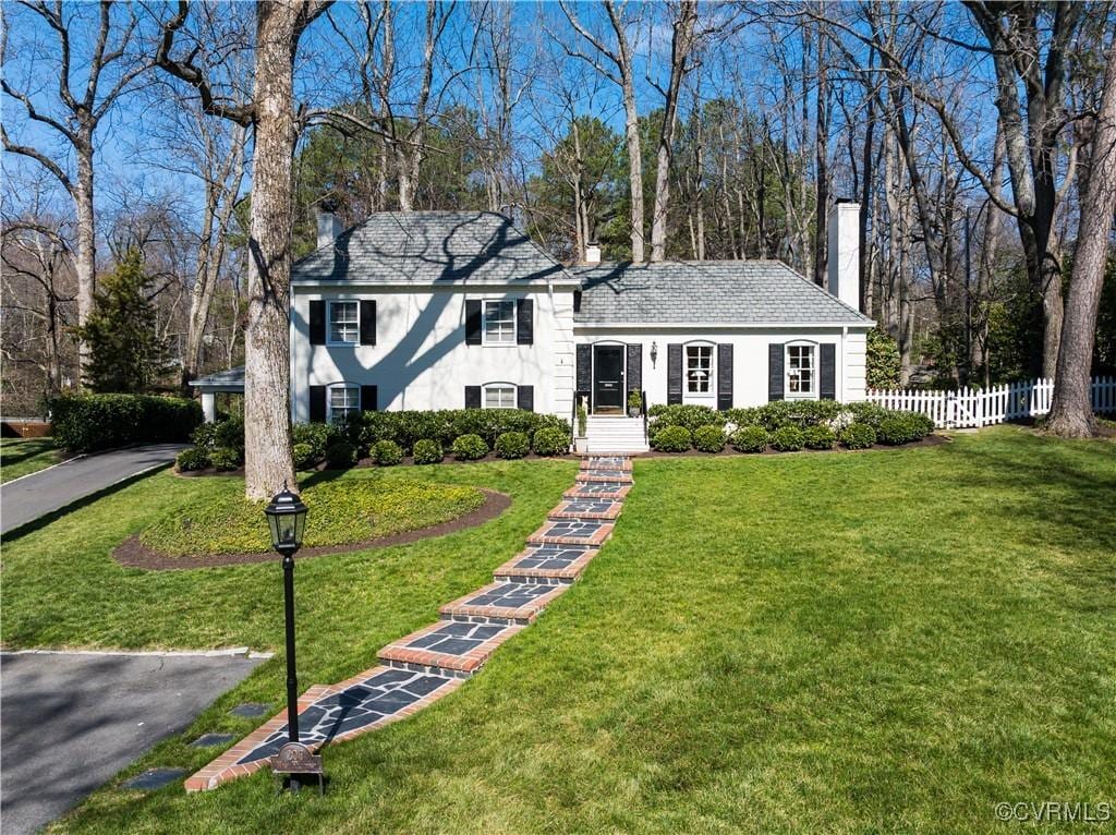 tri-level home with stucco siding, fence, driveway, a front yard, and a chimney