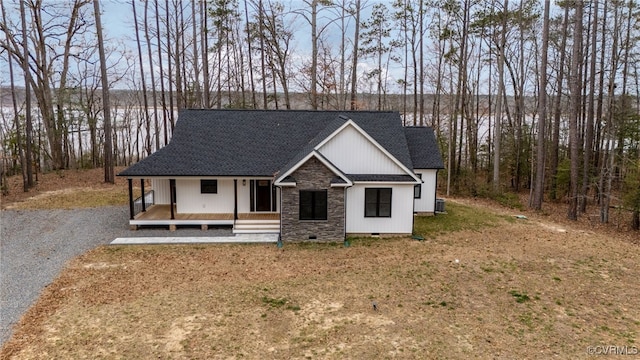 view of front facade with stone siding, covered porch, crawl space, and roof with shingles