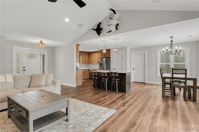 living room with ceiling fan with notable chandelier, baseboards, light wood-style floors, and a healthy amount of sunlight