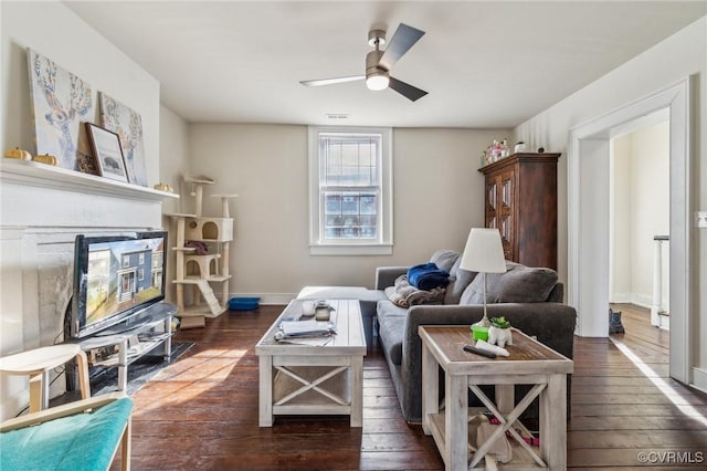 living area with a glass covered fireplace, baseboards, dark wood-style flooring, and ceiling fan