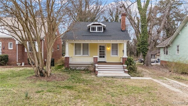 bungalow with a shingled roof, a front lawn, covered porch, a chimney, and driveway