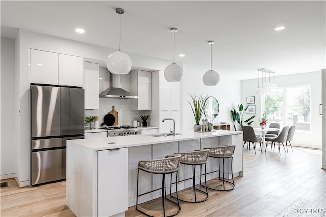 kitchen featuring a sink, wall chimney range hood, freestanding refrigerator, and modern cabinets