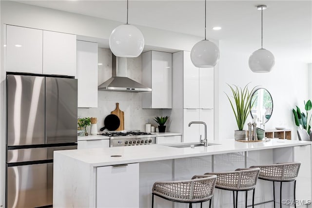 kitchen featuring wall chimney exhaust hood, modern cabinets, a sink, appliances with stainless steel finishes, and white cabinetry