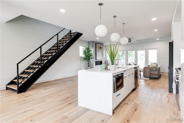kitchen featuring recessed lighting, an island with sink, light wood-style flooring, white cabinets, and stainless steel appliances