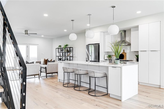 kitchen with modern cabinets, wall chimney range hood, a ceiling fan, freestanding refrigerator, and white cabinetry