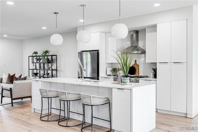 kitchen featuring white cabinets, wall chimney exhaust hood, modern cabinets, freestanding refrigerator, and a breakfast bar
