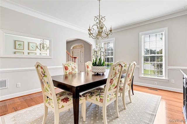 dining room featuring ornamental molding, light wood-style flooring, arched walkways, and a chandelier