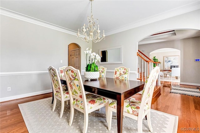 dining room with ornamental molding, wood finished floors, baseboards, and arched walkways